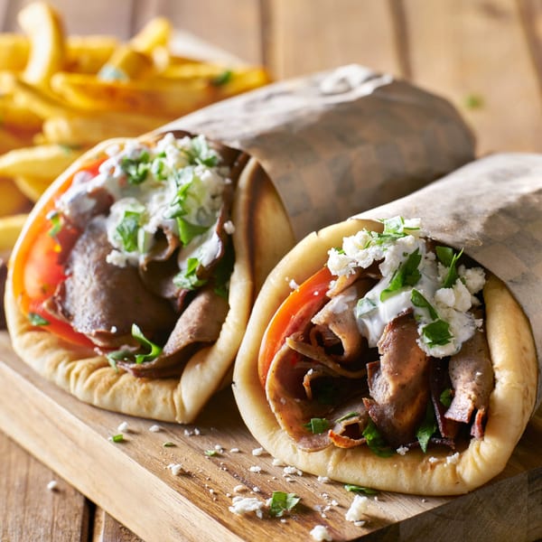Two gyros with meat, tomatoes, feta, and tzatziki sauce, served with golden french fries.